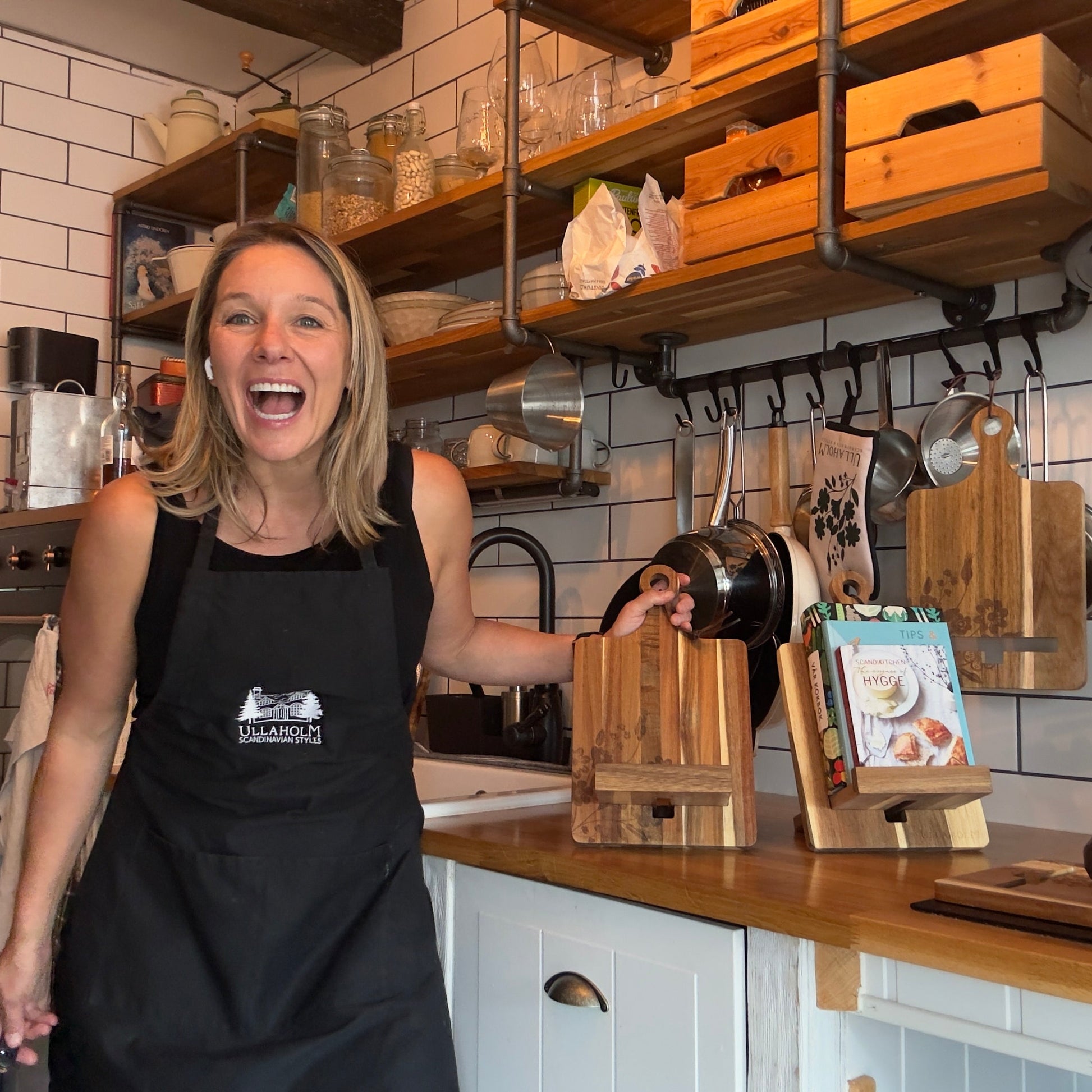 Person in a kitchen wearing an apron, with shelves and kitchenware in the background.